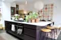 Modern kitchen with black island, potted plants, bar stools, and a colorful quilt on the wall.