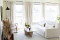An apartment living room with white walls, cream curtains, a white couch, and a white rug