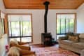 Living room with wood stove, gray sofa, patterned rug, and two brown chairs with fur throws under a wooden ceiling.