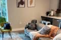 Cozy living room with a gray sofa, patterned pillows, yellow chair, large plant, and abstract wall art.