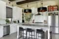 Modern kitchen with white cabinets, stainless steel appliances, black pendant lights, and a large island with bar stools.