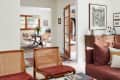 A white living room with brown chairs and a sofa opening up to a midcentury dining room.