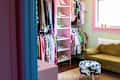 Colorful closet with clothes and shoes, green sofa, cow-print stool, and pink rug in a pastel-themed room.