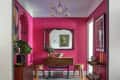 Pink-walled room with a wooden console table, mirror, plants, and framed artwork.