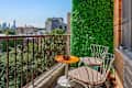 City balcony with orange table, patterned chair, green wall, and view of skyline and trees.