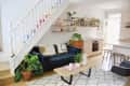Living room with blue sofa, wooden coffee table, plants, and open kitchen under rainbow staircase.