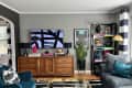 Living room with wooden sideboard, abstract TV art, teal sofa, striped curtains, and decorative shelf with books and sculptures.