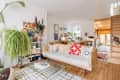 Philadelphia residence with white walls, lots of wood details: living room with tan leather sofa with sherpa seat, red and white throw, shag cream and black rug, clear acrylic coffee table, lots of plants