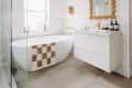 white bathroom with tiled walls, white freestanding tub, and brown and white checkered bath mat