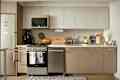 Kitchen with light tan or warm gray cabinets, light wood finish laminate floor, white countertops, small shag area rug, white walls, wood accents, white vases of pink flowers