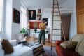 damon d standing in living room. White walls, wood ladder up to loft, large paintings, rust leather sofa, art objects