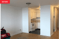 Empty apartment kitchen with white cabinets, stove, and parquet flooring.