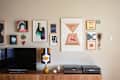 Gallery wall with colorful abstract art above a wooden console, featuring a TV, patterned lamp, and stereo equipment.