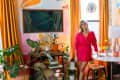 Colorful living room with orange curtains, abstract wall art, plants, and a woman in a red dress by a round table.
