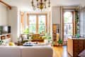 Bright living room with large windows, green armchair, white sofa, plants, and a chandelier.
