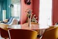 Pink marble table surrounded by yellow dining chairs in pink hued dining room.