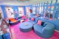 wall of wavy mirrors, neon daisy lighting fixture, blue curved couch, circle ottoman, blue sectional, pink carpet, blue walls