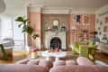 Peach/pink painted art filled living room with a section of floral wallpaper on wall with fireplace.