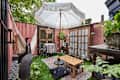 Patio with pink walls, fake grass, wood table with large white umbrella, wood and glass french doors, an off white hammock, bird statues, plants