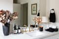 Luxury bathroom products and dried flowers line white vanity top in bathroom.