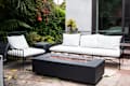 Fire pit as focal point in outdoor seating area with black wrought iron outdoor sofa and chair topped with white cushions.