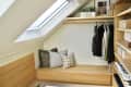 walk in closet with angled ceiling, skylight, wood slat doors, lots of wood details, hanging racks, bench with pillows