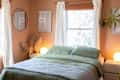 bedroom with peach or pale terracotta walls, bed with pale green bedding, framed art and guitar on wall, arched full length mirror, wood dresser with jewelry, other decor