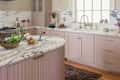Mauve colored kitchen cabinets in renovated kitchen with white and grey marbled countertop and brass hardware. Capiz shell light fixture above island.