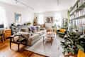 Cozy living room with beige sofa, green armchair, wooden coffee table, plants, bookshelves, and a chess set on a side table.