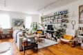 Cozy living room with bookshelves, plants, a gray sofa, wooden floors, and a vintage "Ralph's Ice Cream" sign.