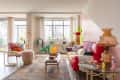 Colorful living room with red sofa, patterned throw pillows, large windows, pink, white, chartreuse, and lavender walls,  wood accent chair with shag throw, wood coffee table with books and colorful design objets
