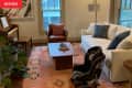 Living room with a white sofa, leather chair, piano, and a car seat on a patterned rug.