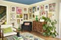 Colorful gallery wall surrounds vintage armchair and wooden dresser in living room.