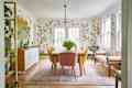 Formal dining room with whimsical, botanical wallpaper and long rectangular wooden table surrounded by yellow upholstered dining chairs.