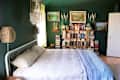 Bedroom with neatly made bed and lots of books on open shelves surrounded by landscape paintings.