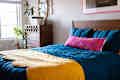 A bed with blue, yellow and pink comforters in a white bedroom.