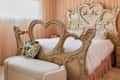 A heart-shaped wooden bed frame with a floral pillow, soft bedding, and sheer curtains in a cozy bedroom.