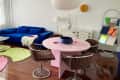 A pink tabling in a white-walled living room with four chairs and a book display stand.