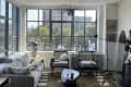 floor to ceiling square paneled windows, grey couch, two white matching arm chairs, green and white geometric outline rug
