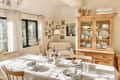 beige dining room with large wood table with pale tablecloth, large wood hutch, cozy corner chair, and gray chandelier