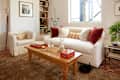 Cozy living room with a white sofa, red and beige pillows, wooden coffee table, and a black rabbit on a patterned rug.