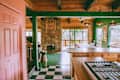 view into home kitchen and dining area with green walls, some wood walls, stone fireplace, and checkered floor
