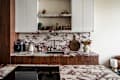 Modern kitchen with marble countertops, wooden cabinets, coffee maker, kettle, and decorative flowers in a vase.