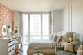 Bright bedroom featuring a floral accent wall, a bed with patterned bedding, a desk with mirrors, and large windows.
