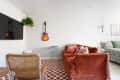 Living room with rust sofa with colorful throw pillows, checkered rug, 2 accent chairs, and wall-mounted TV