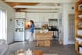 A dweller walls through their kitchen with a butcher block island and white cabinets.