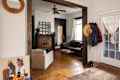 Artwork leaning against wall below round mirror in entry with hanging jackets and area rug, with view of couch and fireplace in living room.