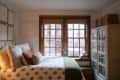 White bedroom with wainscoted walls, vintage furniture, and wood window trim