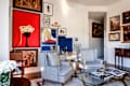Upholstered chairs and glass coffee table in living room with record player and gallery walls.