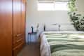 Cozy bedroom featuring a green and white striped quilt, wooden wardrobe, and a small side table with a lamp.